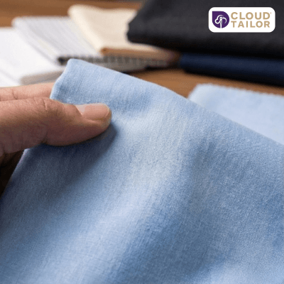 A close-up of high-quality light blue fabric being selected for custom tailored shirts.
